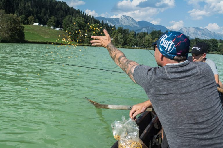 Angler füttert Fische am Putterersee, umgeben von malerischer Natur und Bergen.